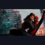 Une femme en manteau sombre est soutenue dans les airs par un personnage masqué en costume rouge et bleu, au milieu d’immeubles urbains flous.